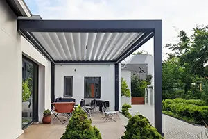 Bioclimatic pergola with rotating sunshade louvers on a modern terrace by a garden with lush vegetation